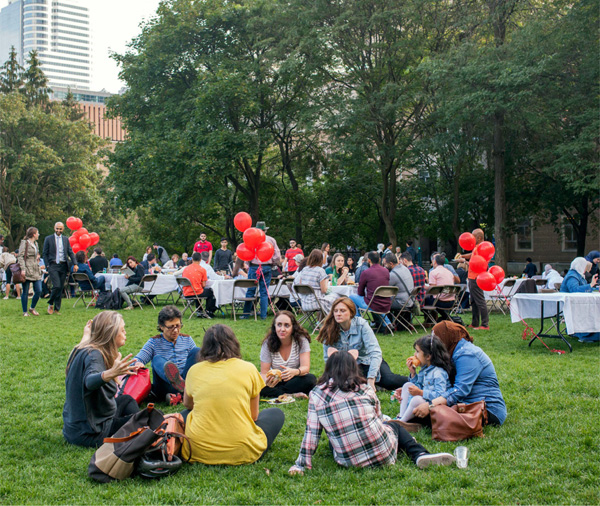 Image of people sitting on the ground and at tables at apicnic in the quad